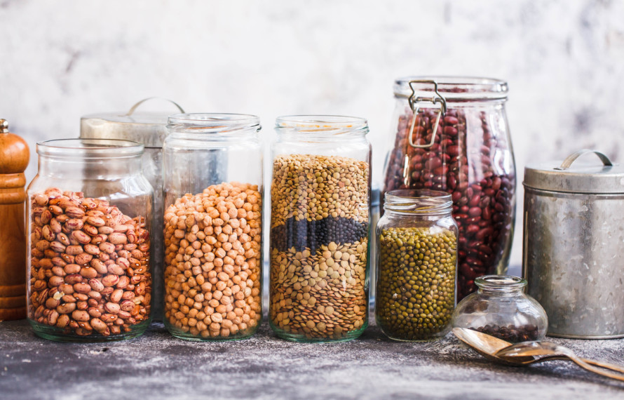 Collection of grain products, lentils, peas, soybeans and red beans in storage jars over on kitchen rural table. Vegetarian products.